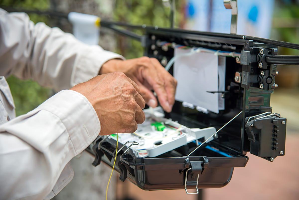 Techniker arbeitet an einer geöffneten Glasfasermuffe im Freien