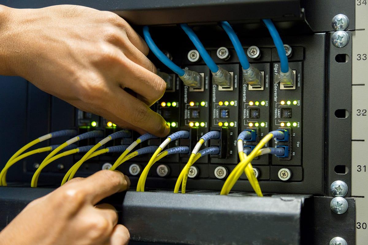 Techniker steckt Glasfaser-Patchkabel in einem Netzwerkschrank