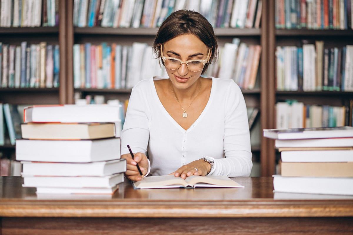 Frau liest an einem Tisch mit Büchern in einer Bibliothek